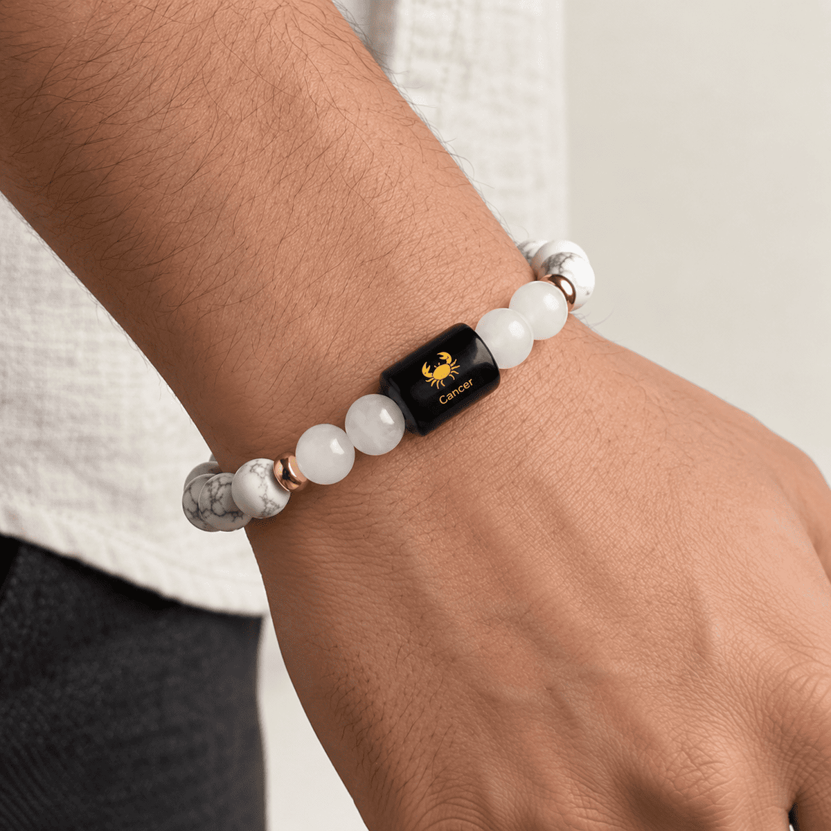 Cancer zodiac crystal bracelet worn on a natural adult wrist featuring Howlite, Milky Quartz, gold spacers and Cancer charm