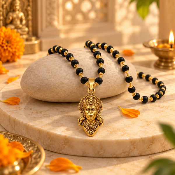 Gold plated Karungali mala with Hanuman pendant displayed on a warm stone surface with flowers and a traditional devotional background.
